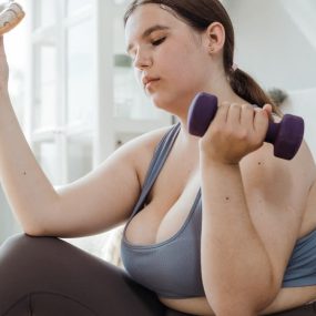A plus size woman in activewear balancing a dumbbell and a donut, symbolizing fitness and indulgence.